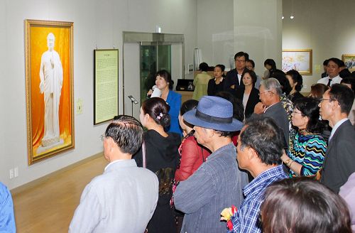 '图2：前来观看美展的各界人士在认真听解说员讲解每幅画的背景。'