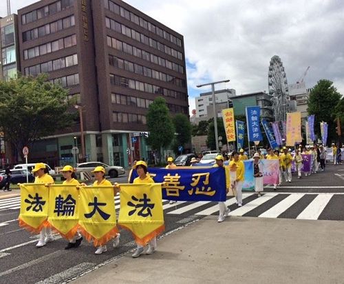 '图1～2：八月五日（星期六），法轮功学员们从早上七点开始在爱知县名古屋市中心的荣公园（Sakae Park）炼五套功法，之后在最繁华地区的荣（Sakae）举办游行。游行队伍由精神抖擞的天国乐团引领，其后是打着“法轮大法好”、“真善忍”、“呼吁停止迫害法轮功”等横幅的队伍。'