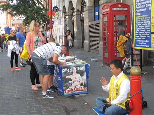'图2：在伦敦唐人街，“反迫害二十周年”游行队伍让一对英国夫妇第一次看到法轮功真相，他们马上来到法轮功学员在唐人街讲真相点继续了解真相，并签名支持制止迫害。'