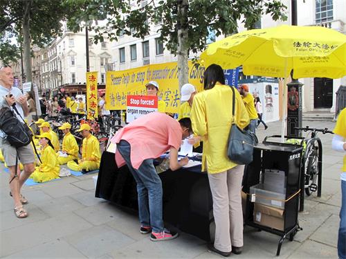 '图5：二零一九年七月二十日，在伦敦圣马丁广场，一位在英国留学的香港青年听法轮功学员讲真相，在法轮功反迫害征签表上签名。'