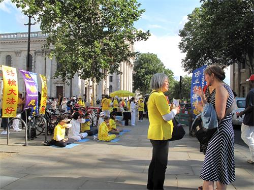 '图7：二零一九年七月二十日，在伦敦圣马丁广场，这女士（右）被法轮功功法演示所吸引，询问学员真相，并在反迫害征签表上签了名。'