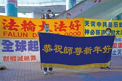 '图1：无惧打压，法轮功学员坚持讲真相，希望更多世人选择良知。在红磡真相点讲真相的法轮功学员恭祝李洪志先生新年快乐。'